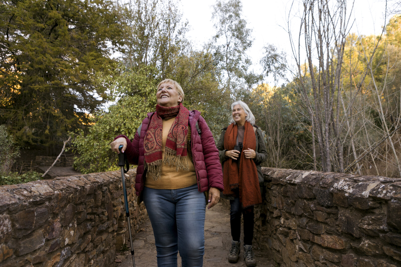 dos-mujeres-mayores-cruzando-un-puente-de-piedra-mientras-estan-en-la-naturaleza